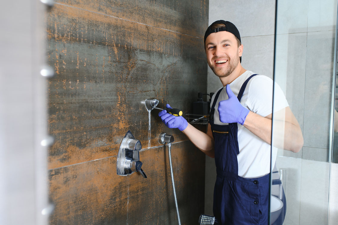 a person in a blue uniform and gloves holding a screwdriver fixing a shower