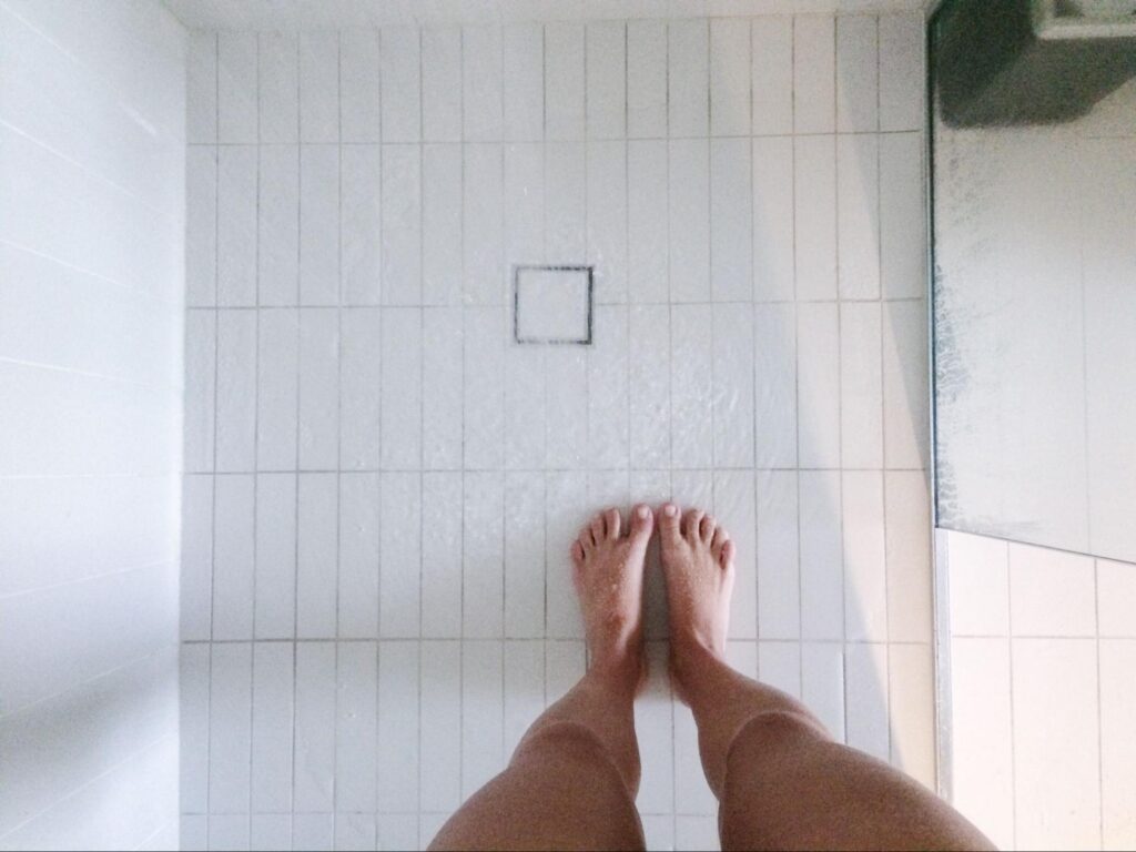 View of a woman’s legs as she stands in a tiled shower.