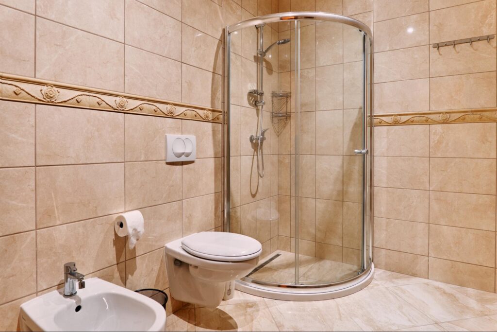 A view of a glass cabin shower in the corner of a beige-toned bathroom.