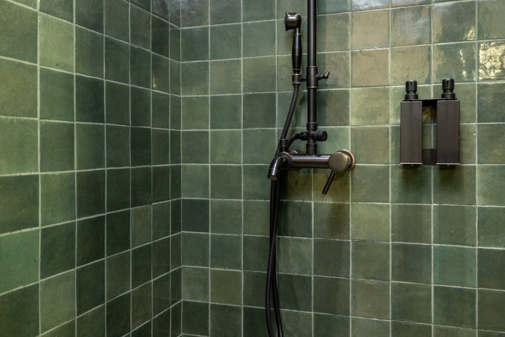 A shower stall tiled with jade green tiles and dark gray hardware.