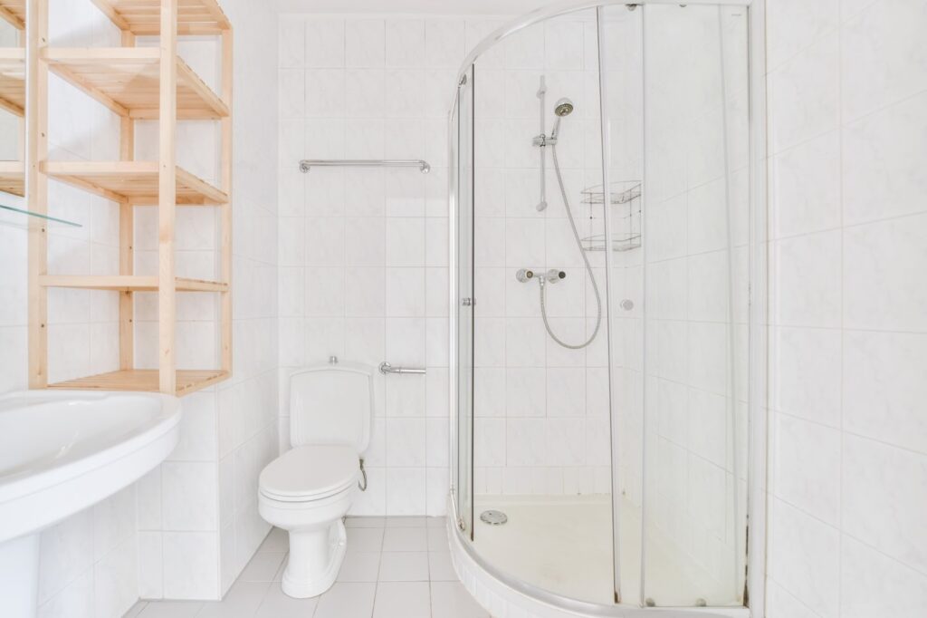 A walk-in shower in a bathroom with white floors and white tiling. 