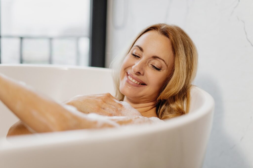 A smiling woman relaxes in a bubble bath.