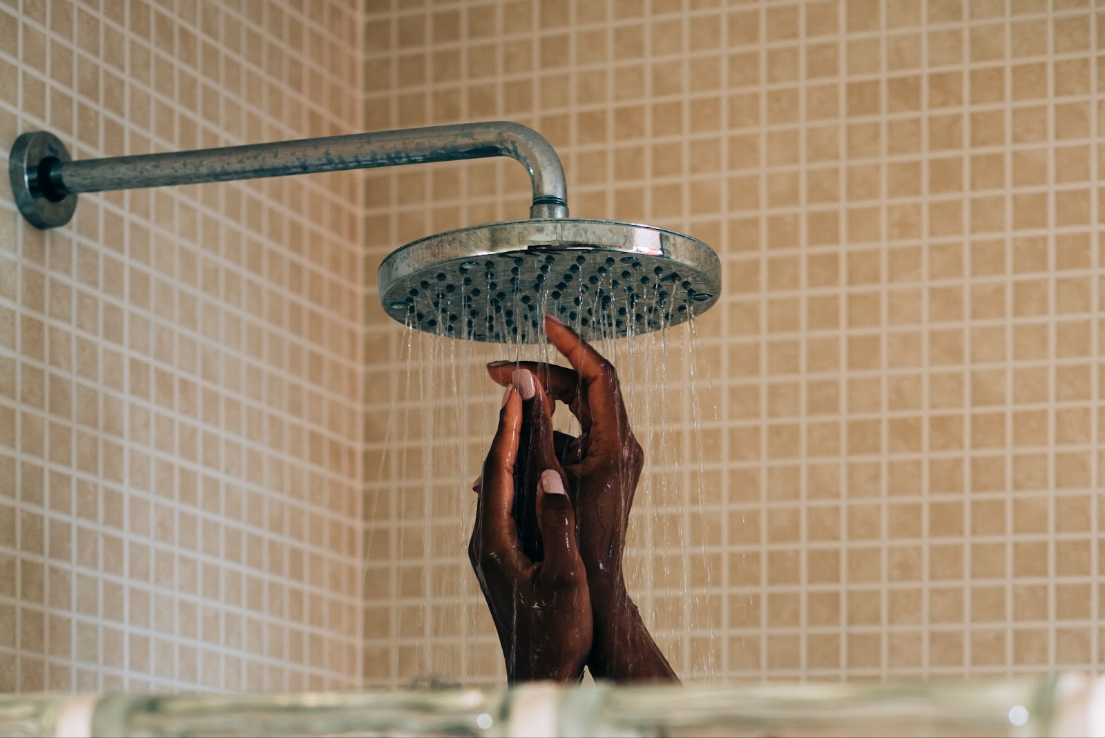 A woman’s hand reaching up to touch a shower head. 