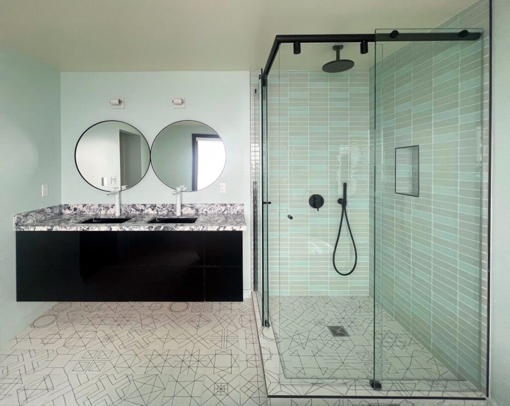A modern minimalist bathroom featuring a glass shower enclosure, dual round mirrors, and his-and-hers sinks, showcasing sleek design aesthetics.