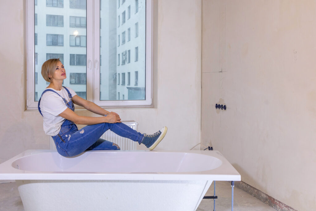  woman is assessing her bathroom while sitting on the edge of a bathtub.