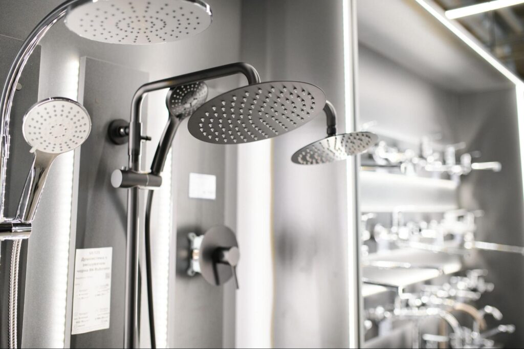 Assorted shower fixtures, bathtub mixers, and washbasin taps displayed in a hardware store, including a sink with a tap.